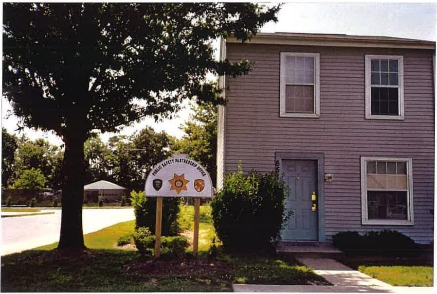 A gray end townhouse at Carroll LaPlata Village with a blue front door, shaded by a large tree