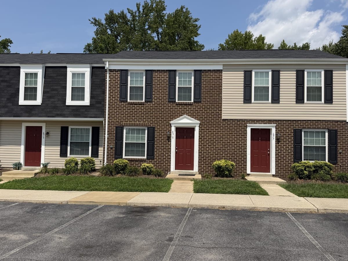 A straight-on view of a townhouse row at Carroll LaPlata Village, brick and beige siding with black shutters and red doors