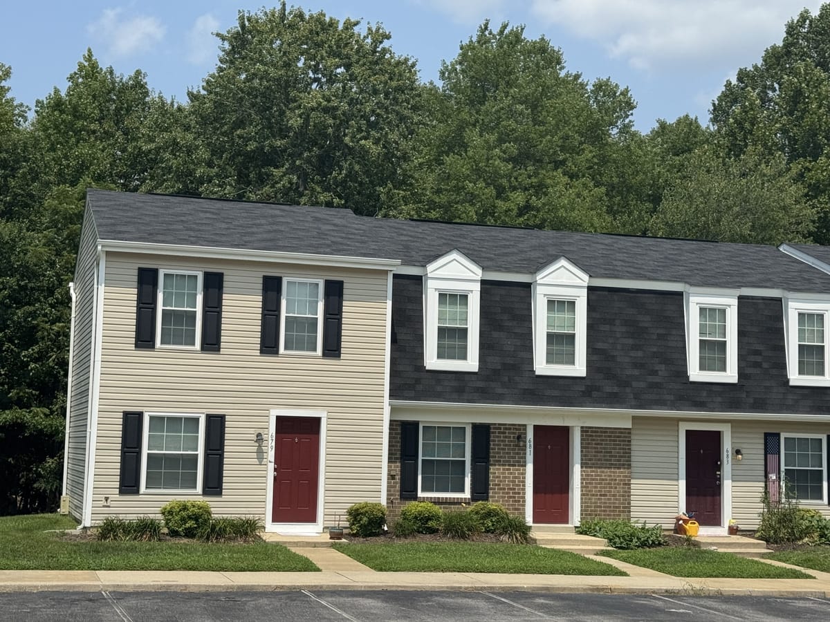 A row of two-story townhouses at Carroll LaPlata Village set against tall trees, with dormer windows, foundation plantings and a front walk
