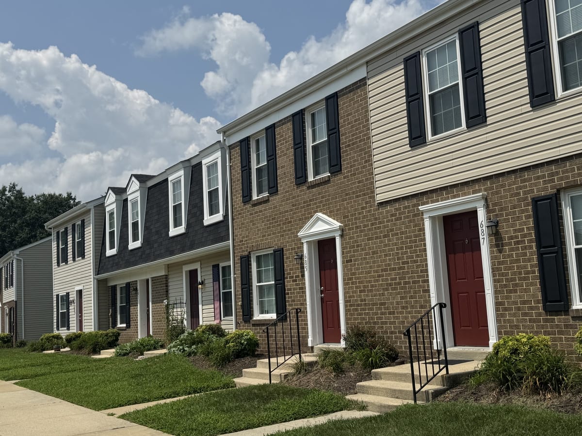 An angled view of brick-front townhouses at Carroll LaPlata Village with iron stair rails, dormers and planted beds