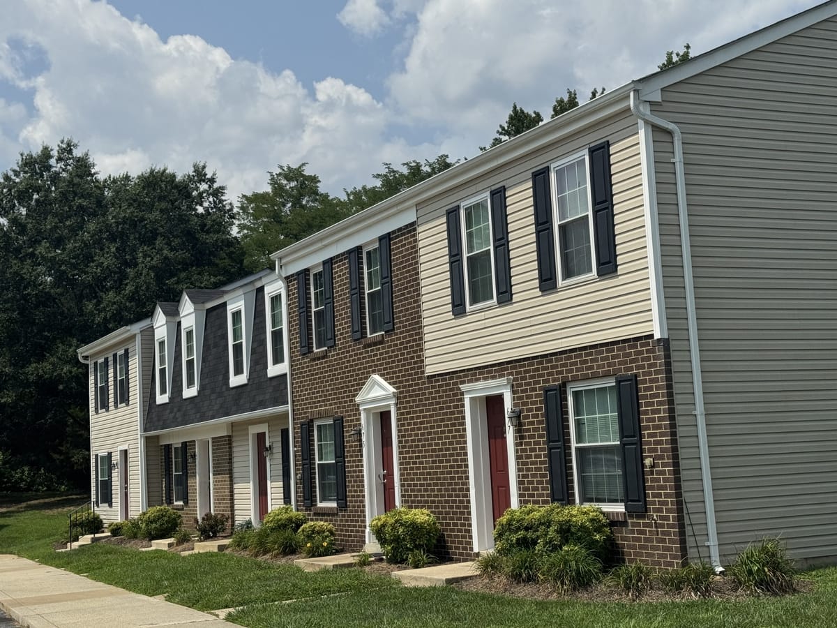 Two-story townhouses at Carroll LaPlata Village with brick and siding, black shutters and red doors under a blue sky