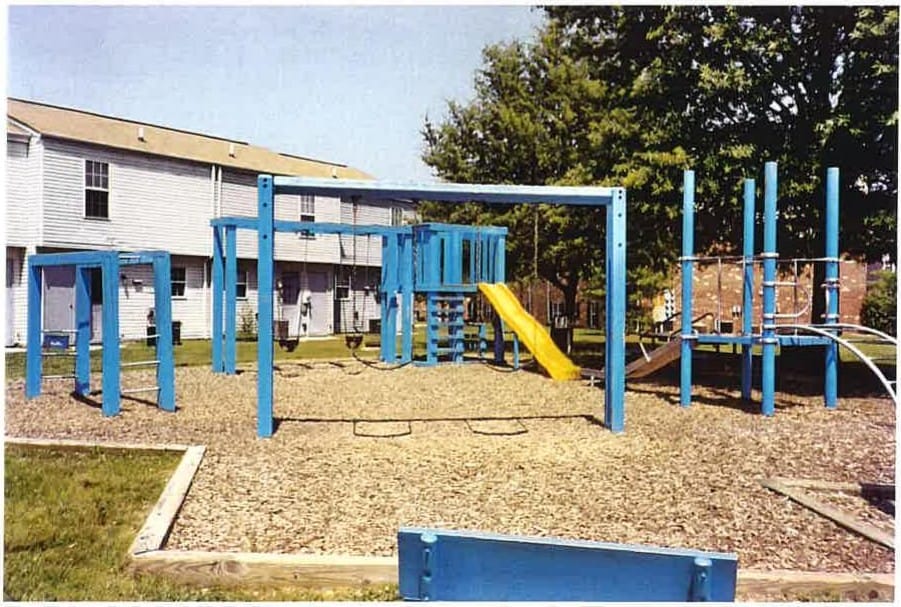 The community playground at Carroll LaPlata Village, with blue climbing equipment and a yellow slide beside the townhouses