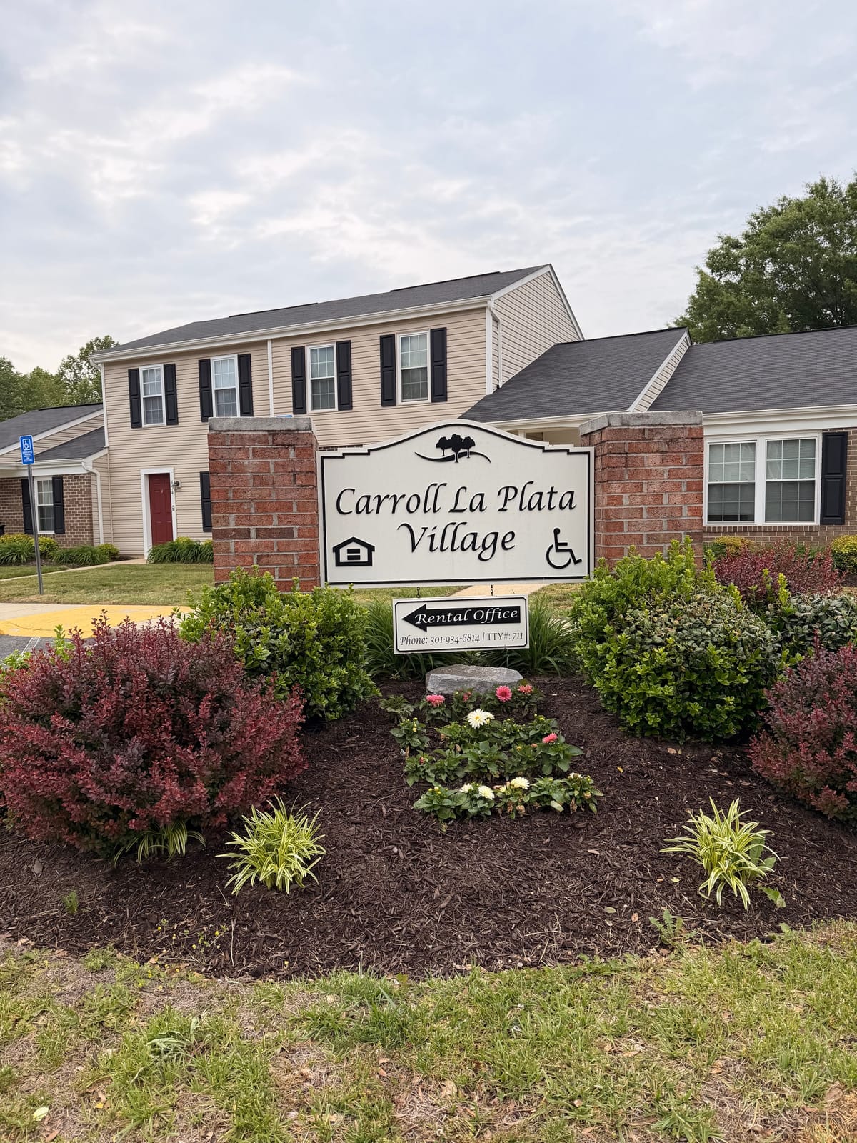 The Carroll LaPlata Village entrance sign between brick pillars, with a rental-office arrow sign below and townhouses behind
